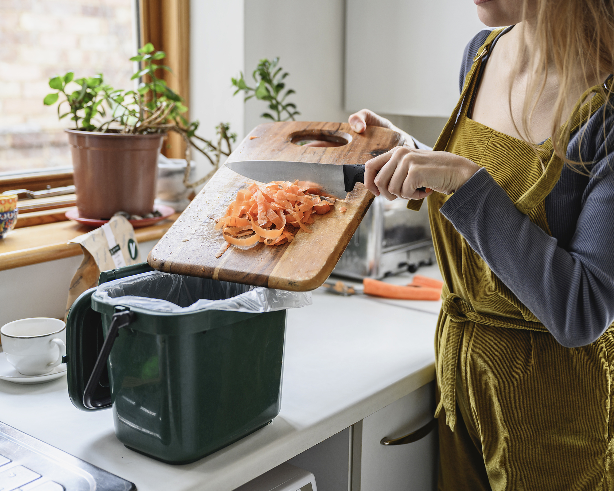 Woman tips carrot peelings into countertop compost bin