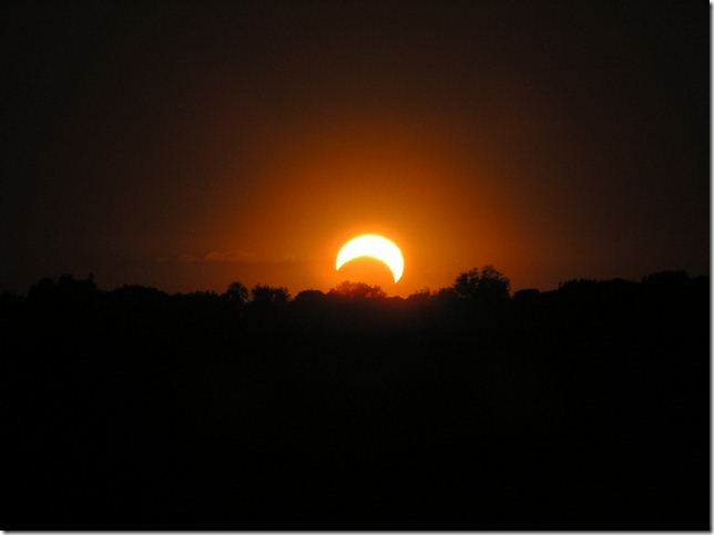 A dark landscape over which there is a fiery sphere that appears to have a large chunk 