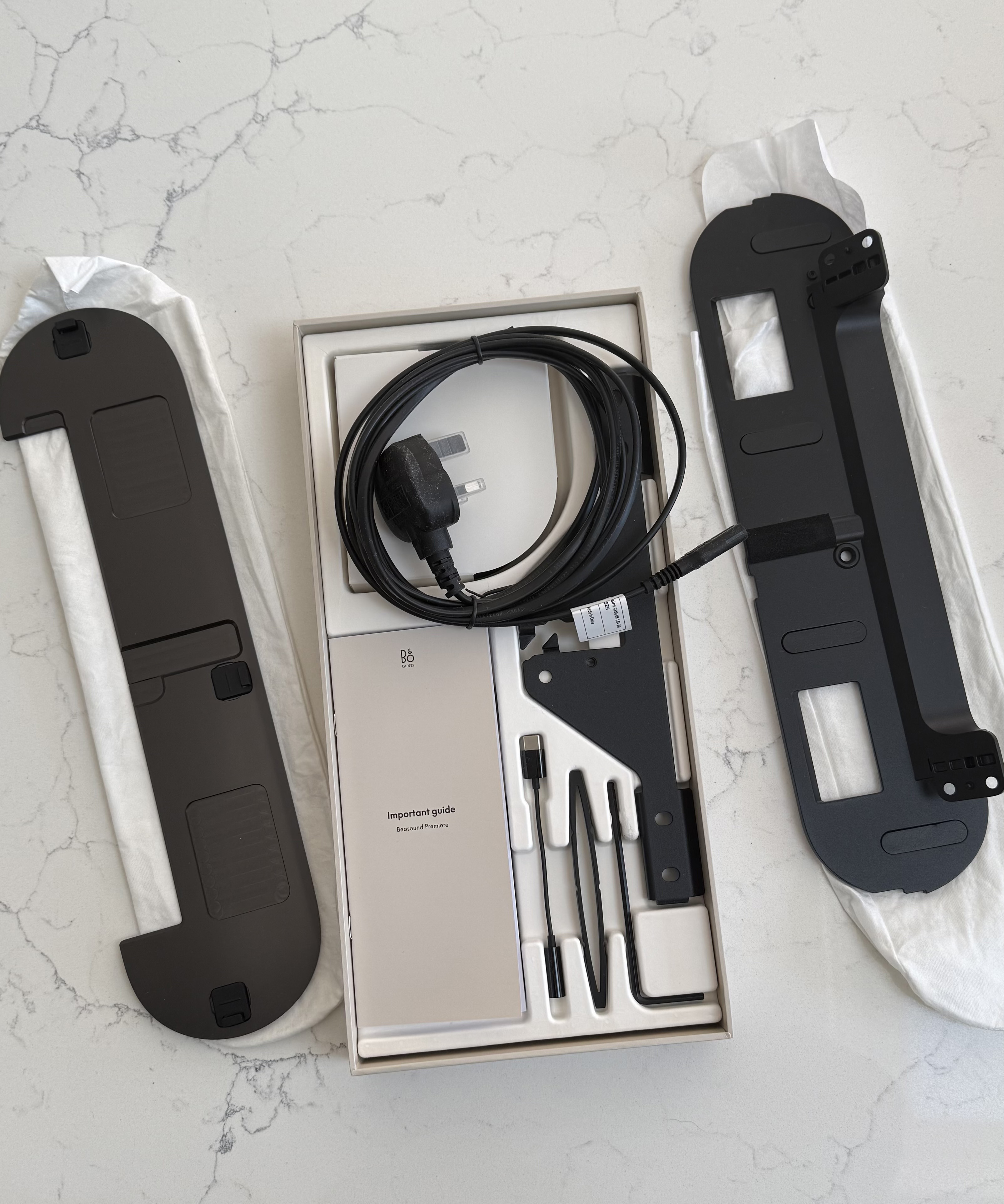 Unboxed wall mounting kit components laid out on a surface, including brackets, screws, cables and instruction booklet