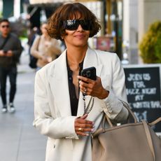 Halle wears a white blazer, black top, and a tan bag.