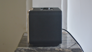 The JBL Authentics 200 speaker on a sits on a small marble surface. We can see its side of plan black plastic.