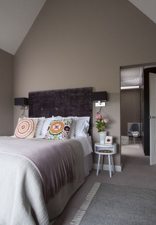 neutral bedroom with a statement headboard, bold cushions, wall lights and a bedside table