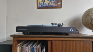 The Victrola Hi-Res Onyx turntable on a wooden sideboard with records underneath and a globe next to it.