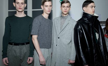 Four male models wearing looks from Jil Sander's collection. Three models are wearing green and grey trousers, tops and a jacket. And one model is wearing a black leather coat