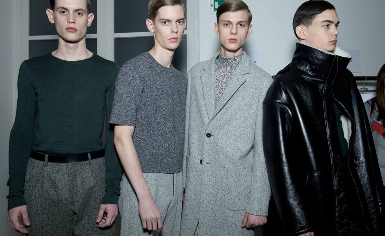 Four male models wearing looks from Jil Sander&#039;s collection. Three models are wearing green and grey trousers, tops and a jacket. And one model is wearing a black leather coat