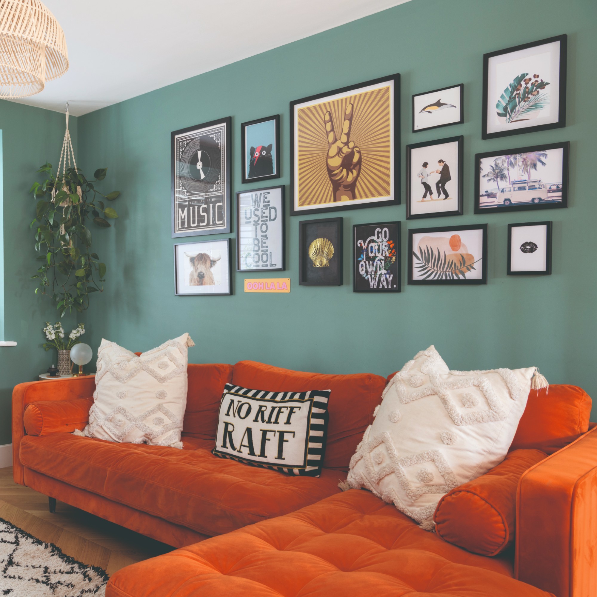 A mint green-painted living room with a orange velvet chaise sofa and a gallery wall above it