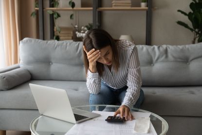 Young woman sitting on sofa calculating payments