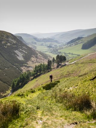 View of a verdant valley in wales with a solo hiker walking up a path