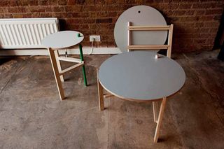 Round three-legged tables in ash, powder coated steel and plywood on display photographer with brick concrete walls in the background