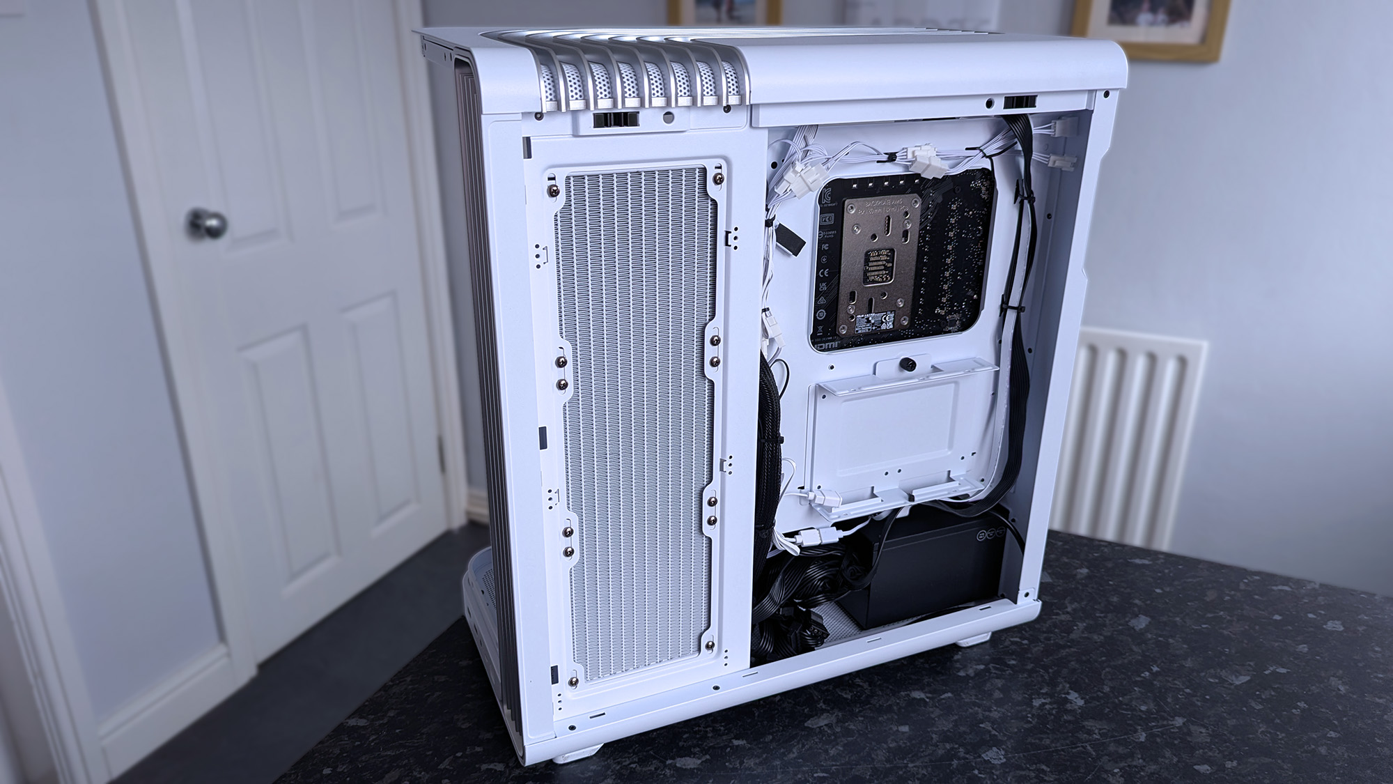 A white iBUYPOWER RDY Trace X R01 computer case is open, showing internal components and cable management. It sits on a dark countertop.