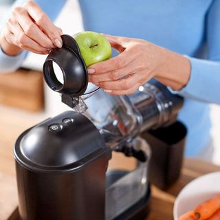 a woman in a blue top putting a green apple in a Philips Viva Cold Press Masticating Slow Juicer