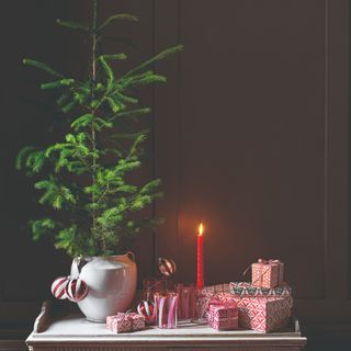 A tabletop Christmas tree next to a lit candlesticks and a pile of small presents