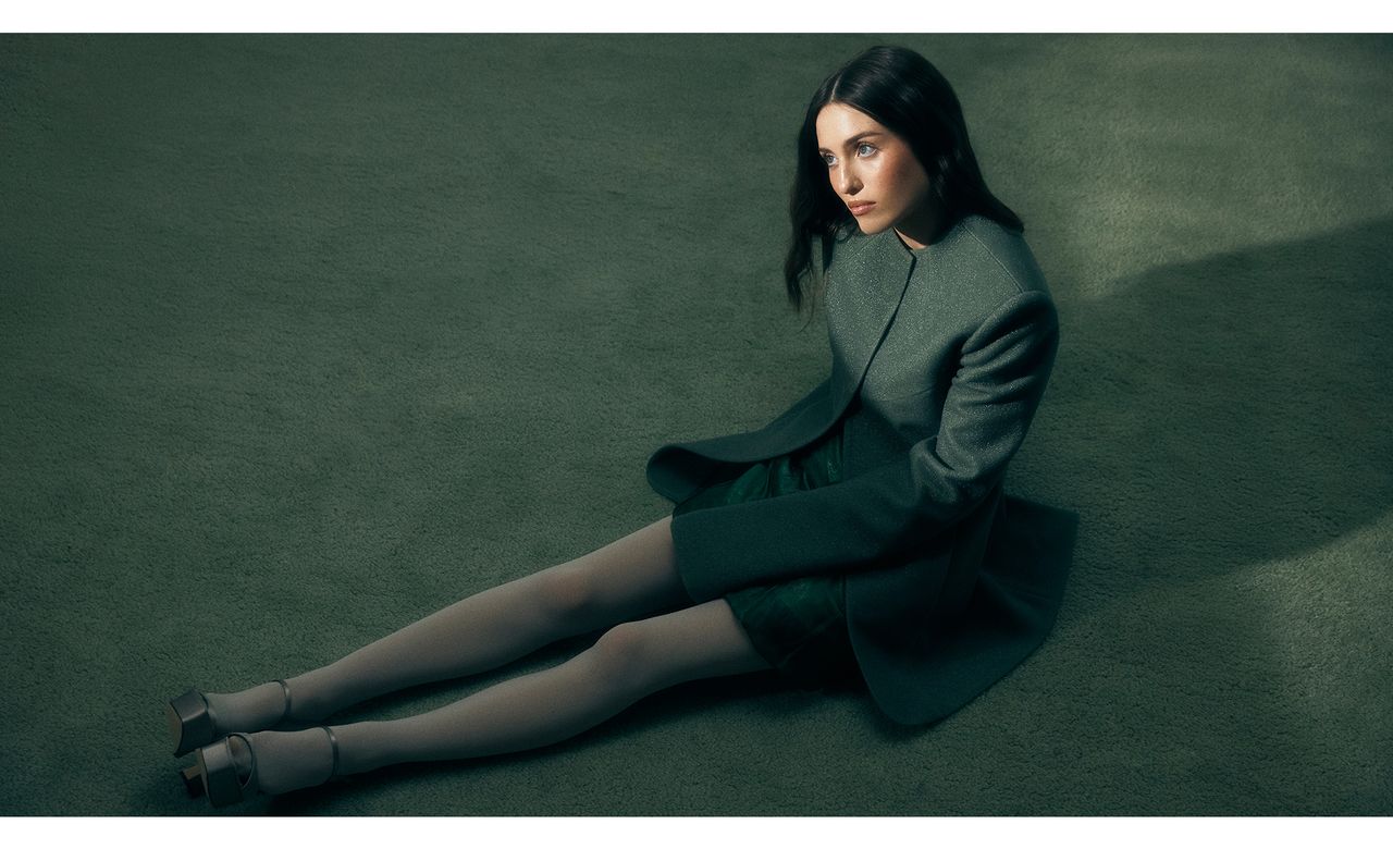 Madeline Argy sitting on green carpet wearing a green jacket and dress by Tory Burch