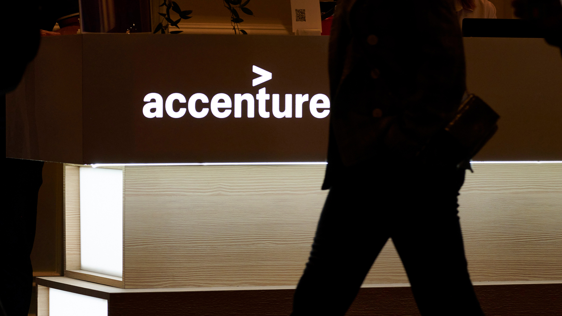 Illuminated Accenture logo pictured at CES 2026 in Las Vegas, with silhouetted man walking past in low light.