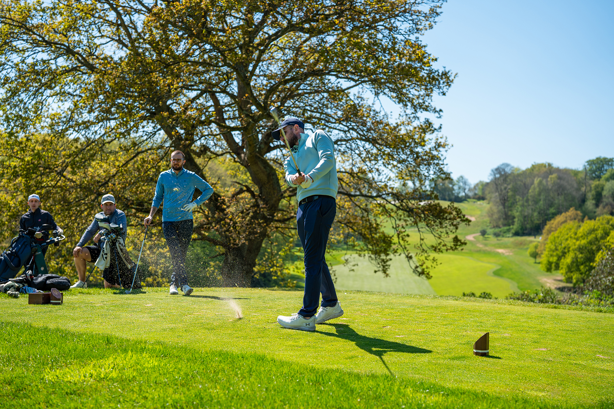 Baz Plummer just through impact hitting a golf shot, watched by three playing partners as he tried to break 90 for the first time ever