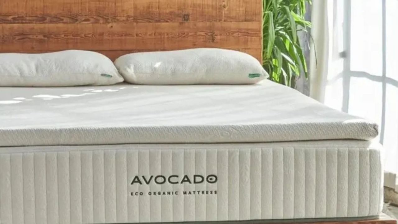 Avocado Eco Organic Mattress Topper on a wooden beside a window covered with a sheer curtain. 