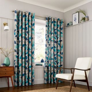 Mixed blues on floral design full length curtains, with warm gray wall paneling.