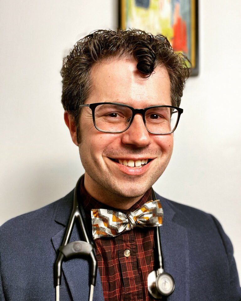 Dr Zachary Rubin smiling at the camera, wearing a colorful bow tie and a stethoscope around his neck
