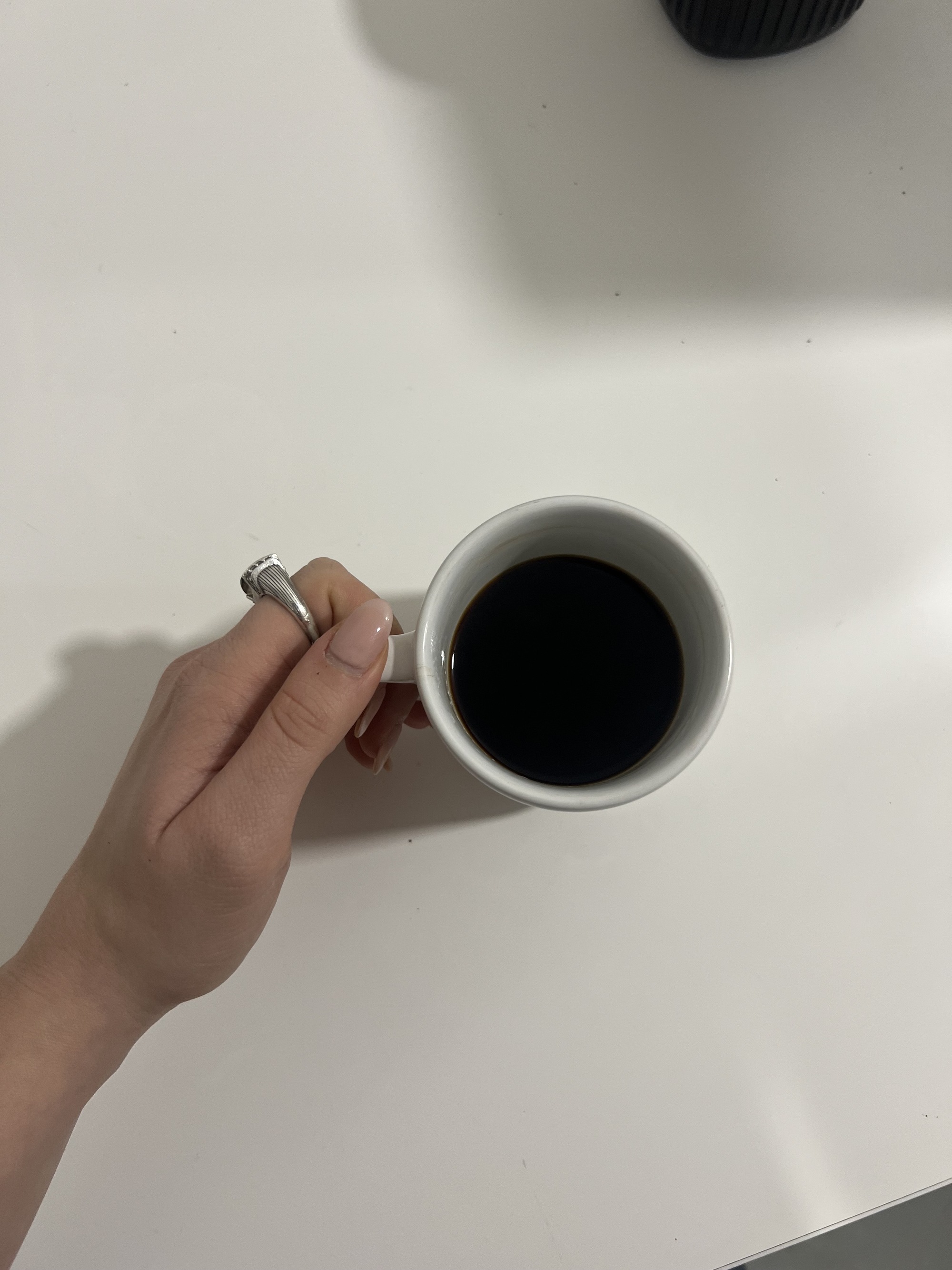 Image from above of a hand holding a mug of coffee on a white countertop.