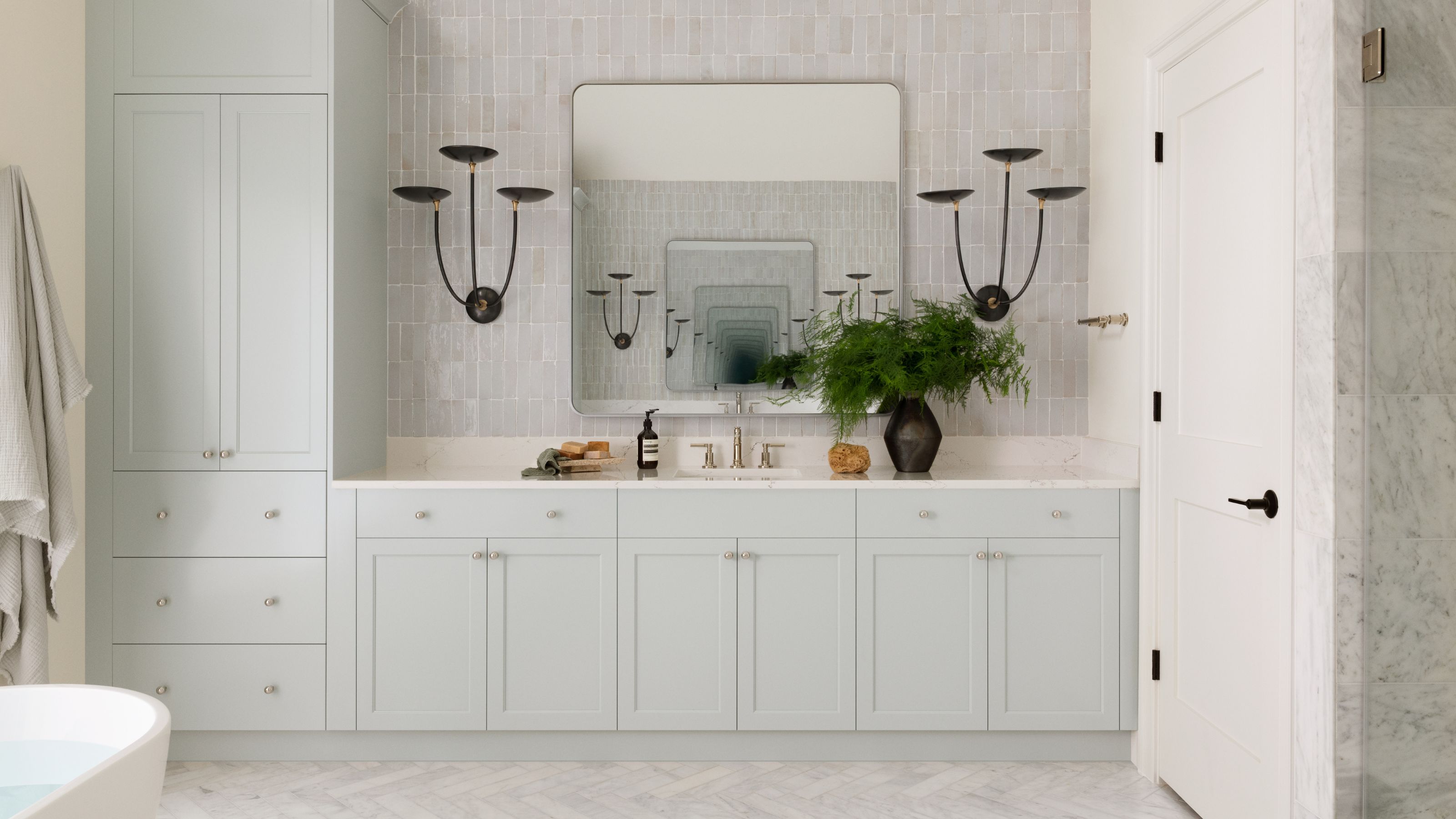 A wide, light green double vanity with a marble countertop, large rectangular mirror, and two sculptural black wall sconces.