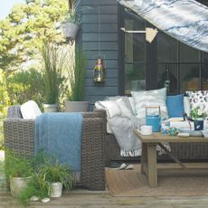 Grey rattan garden furniture on decking area with blue cushions and throws