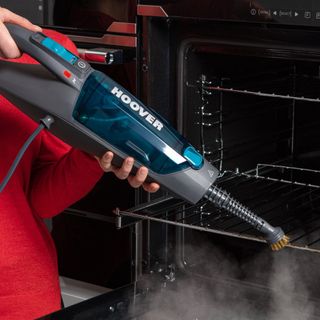 Closeup of a handheld hoover steam cleaner being used to clean an over rack.