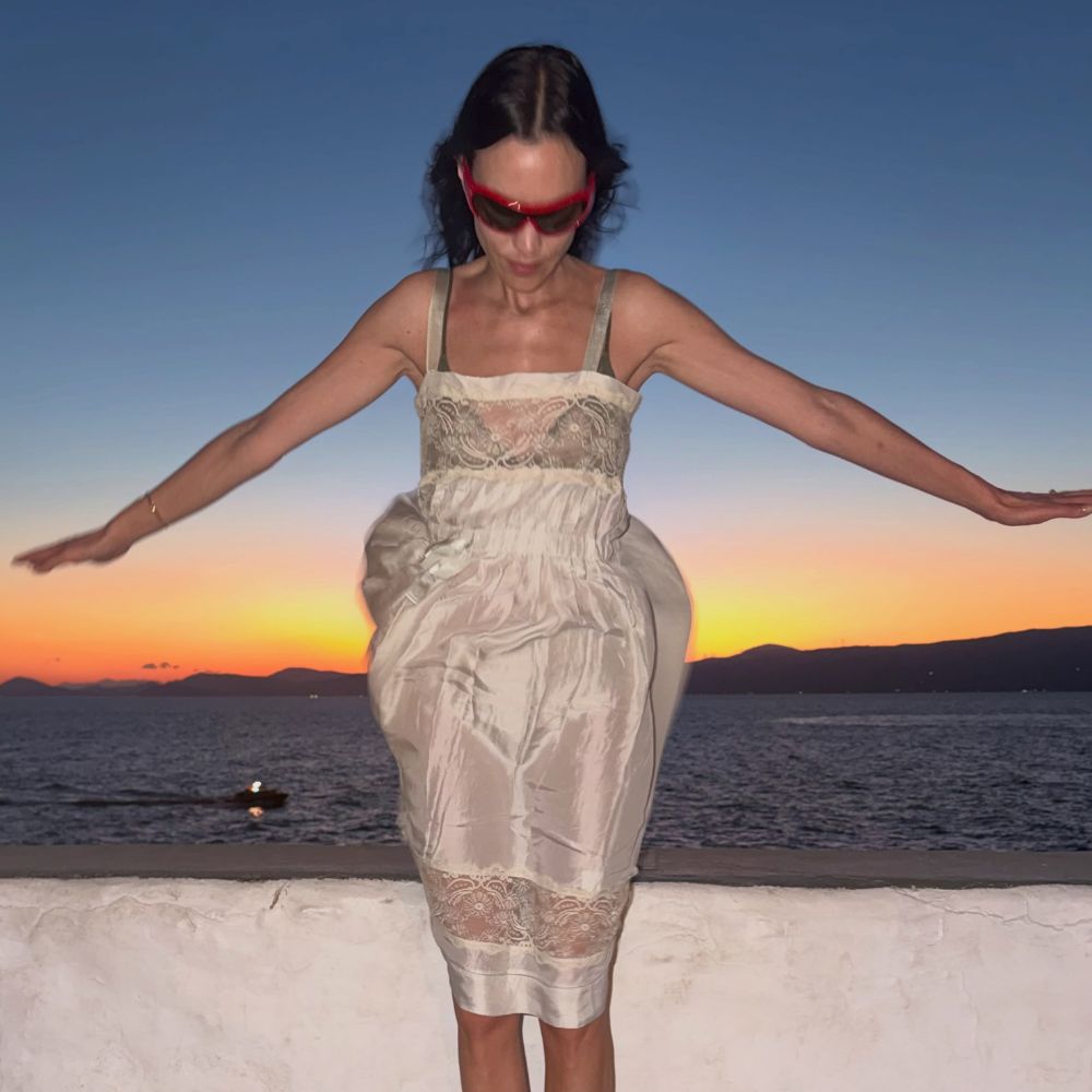 Alexa Chung wears a white lace-trim knee-length dress with white ballet flats and red sunglasses.