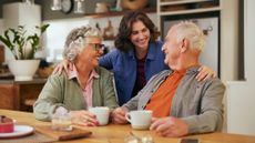 Daughter embracing senior parents sitting at table