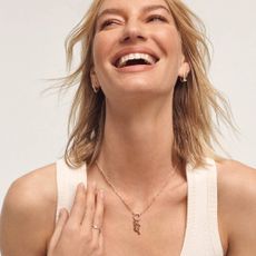 A happy woman smiling, wearing a charm necklace, a gold ring, and matching gold hoop earrings from Kay Jewelers. 