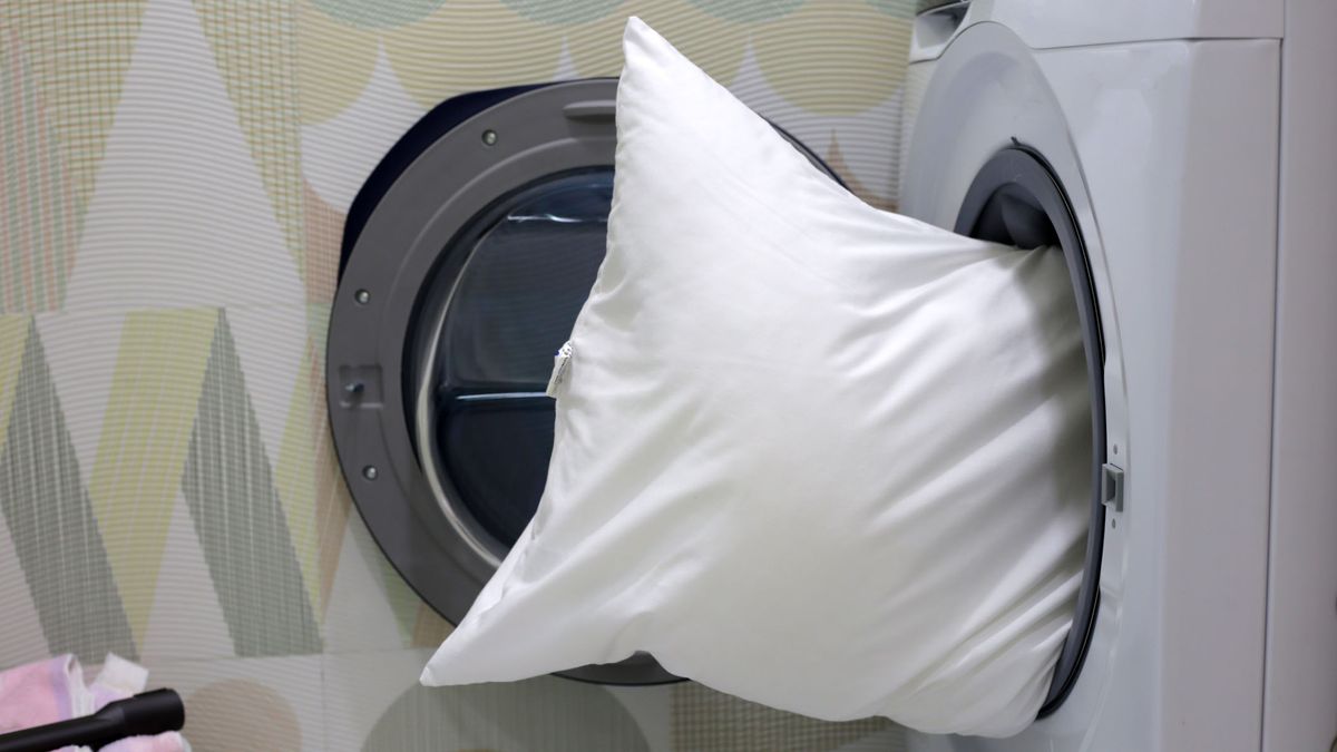 Image shows a white pillow being placed inside a washing machine for washing