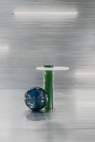 The deep blue ball-shaped volume is leaning on the deep green cylinder-shaped volume, which supports the white table top and emerges on top of it.