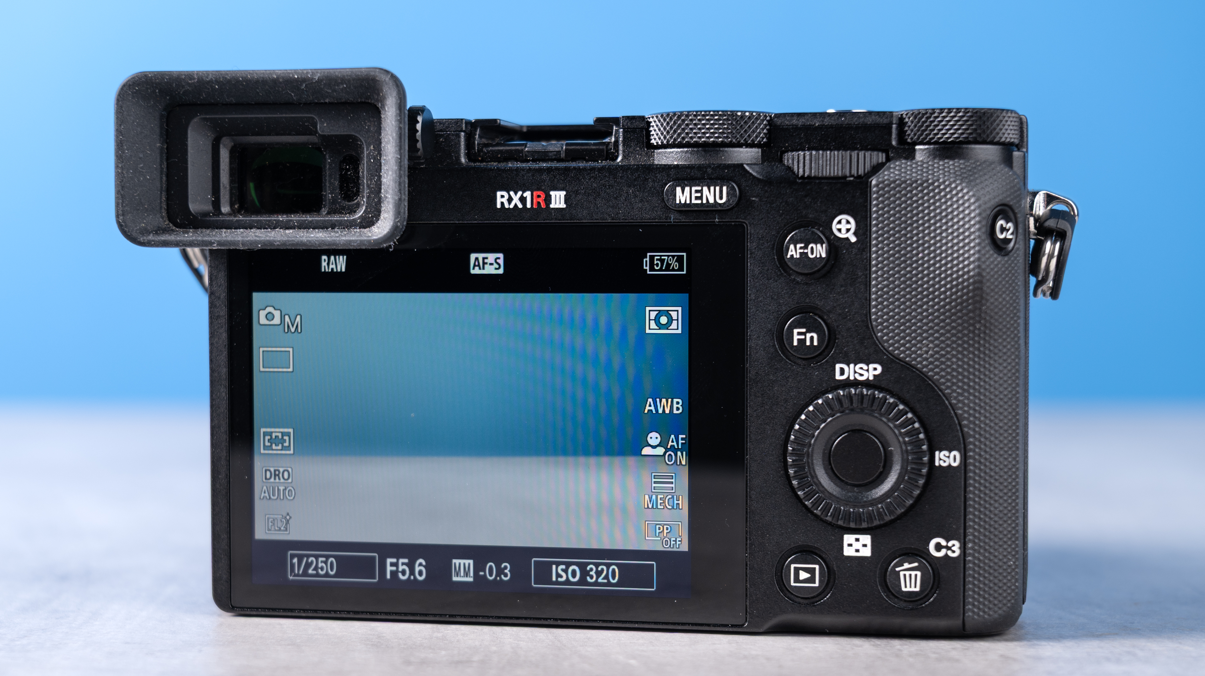 A photo of the Sony RX1R III rear, the camera is on a stone surface with a blue background