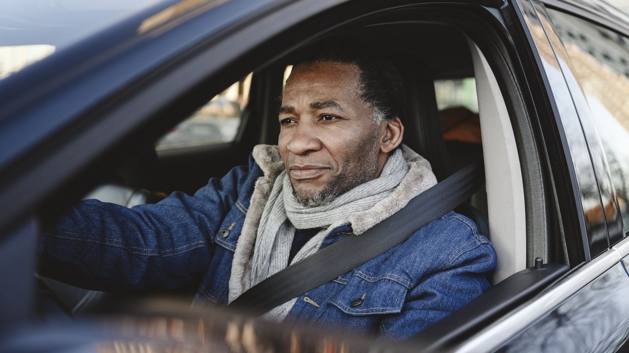 An older man in the driver&#039;s seat of a car.