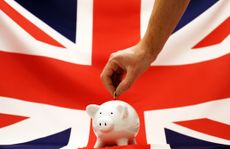 A man placing a coin in a white piggy bank against a union jack background.