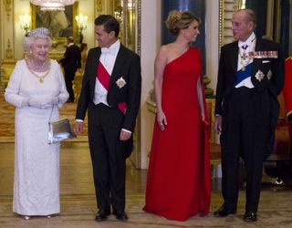 Queen Elizabeth wearing a diamond tiara and white evening dress talking to the president of mexico while the first lady, in a red gown, talks to Prince Philip