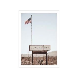 A wall art print with a blue sky and a white and brown sign that says 'Howdy Honey' with an American flag hanging above it on a pole