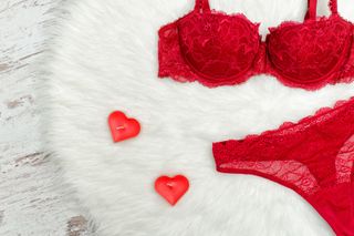 A red lacey underwear set on a fluffy background with red heart shaped candles.