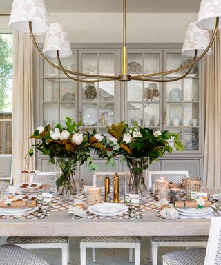 fall dining tablescape with glazed shelving unit behind table, cream drapes, chandelier with fabric shades, flowers, Thanksgiving table, crackers, table settings ideas