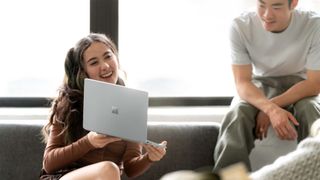 A woman showing off a Microsoft Surface Laptop Go to an man sitting on a couch