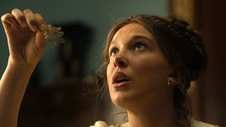 Millie Bobby Brown looking up and holding something in her hand in Enola Homes 3