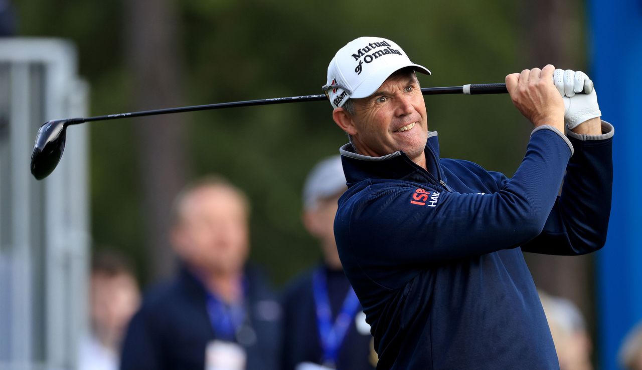 Padraig Harrington watches his tee shot whilst wearing a blue midlayer