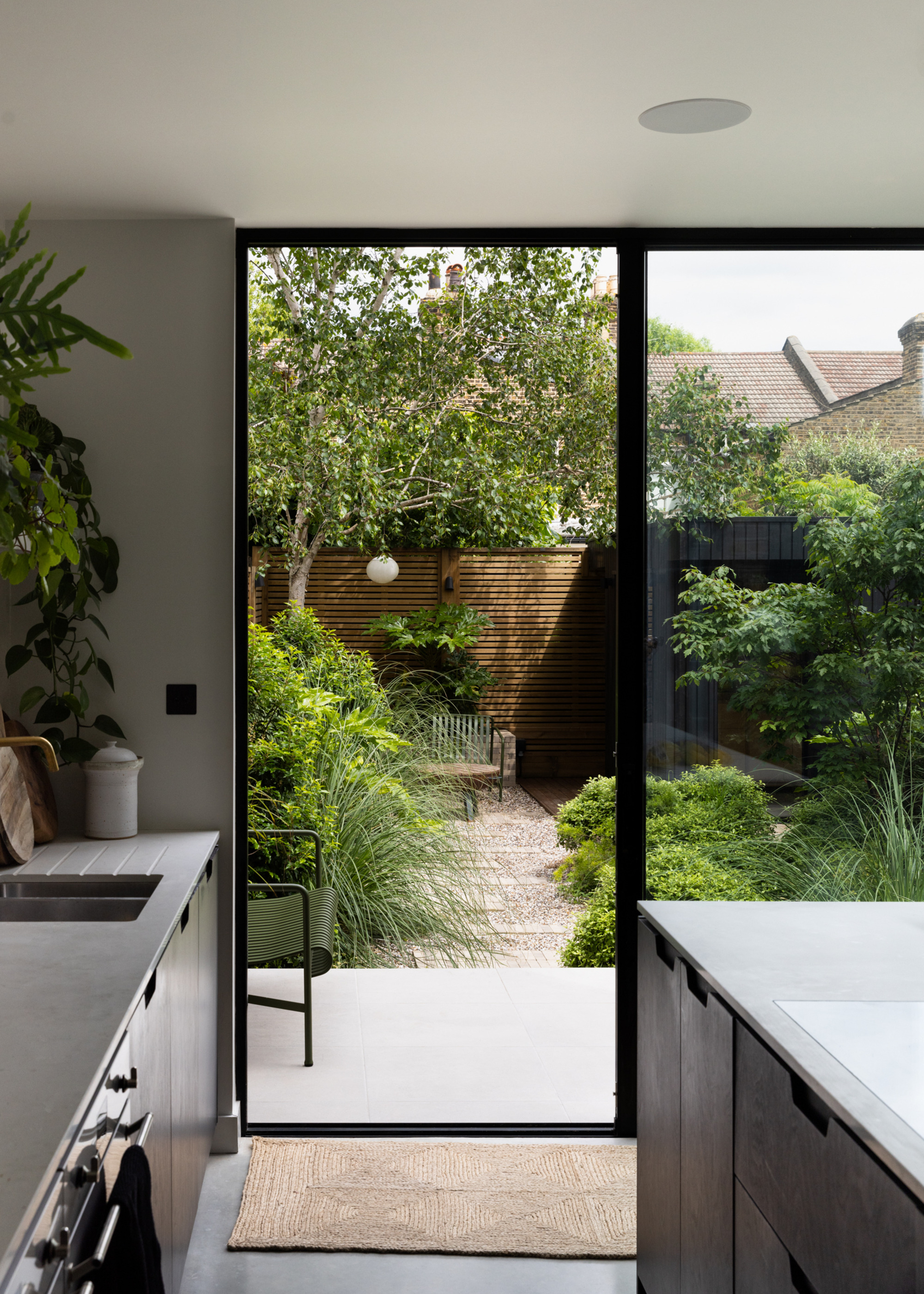 view of patio in a small garden with lush plantings through glass sliding doors