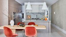 modern kitchen with timber cabinets, blue marble backsplash, plaster walls, two white pendant lights over the counter, with timber dining table in front with orange velvet chairs, with vases on table