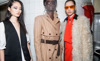 Model is seen wearing a beige pinstripe coat with belt, another wears a cream shearling jacket and red shirt