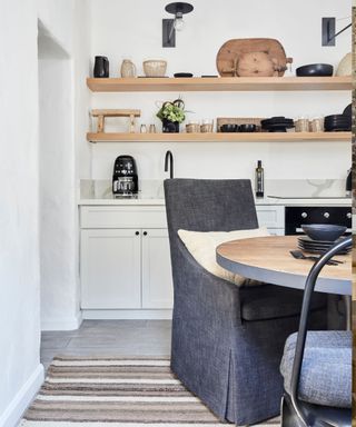 Modern rustic kitchen with open shelving, white cabinets, circular wooden dining table and linen chairs
