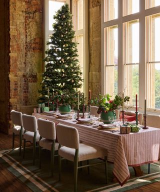 large dining hall with stone walls and windows decorated for christmas with a tree and festive tablescape with striped tablecloth