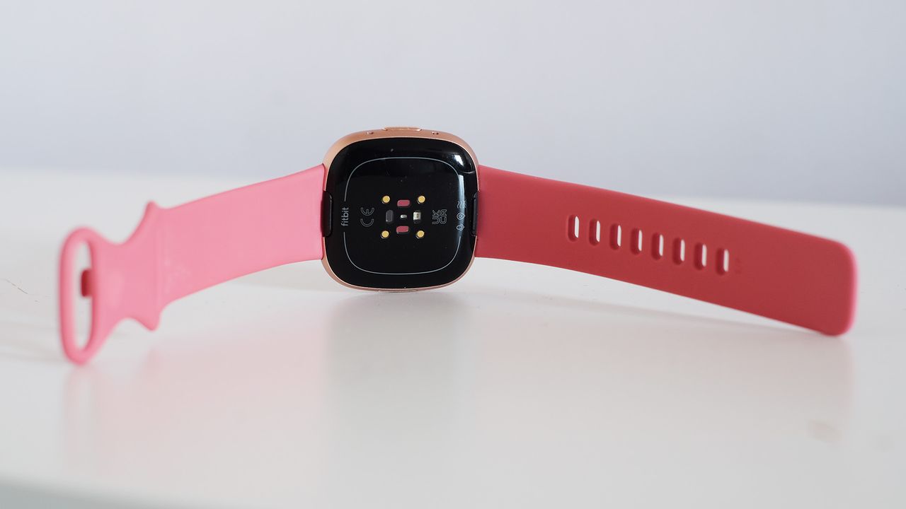 Back of the Fitbit Versa 4 with pink strap on white table