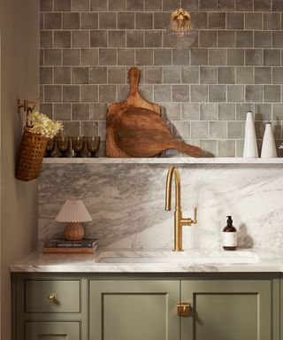 A green kitchen with marble backsplash, tiled walls and a gold faucet