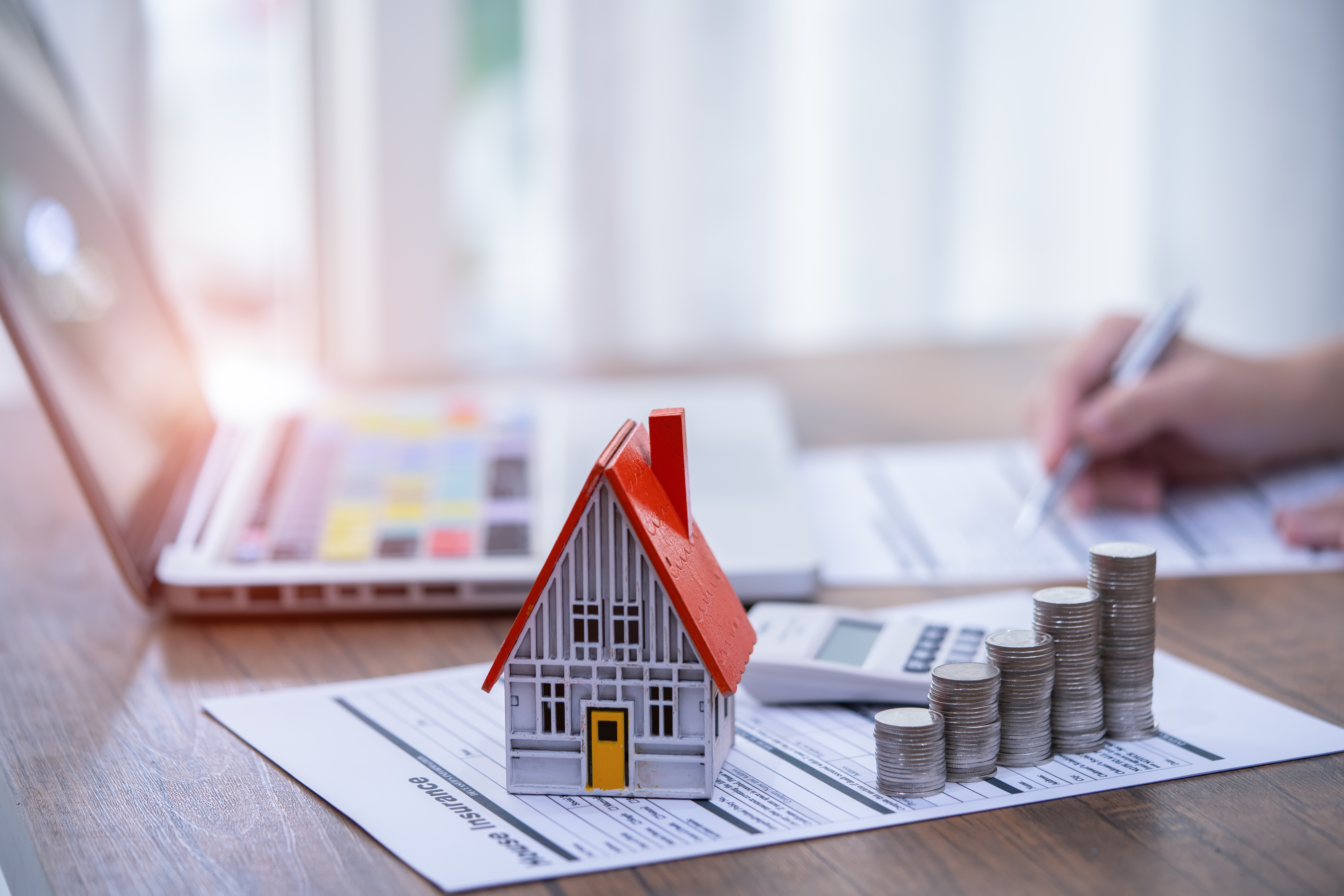 Landlord's hand pictured beside money, calculator, laptop and property figure as they look at finances.