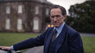 Bertie Carvel in a dark suit as Dalgliesh stands outside a country house.